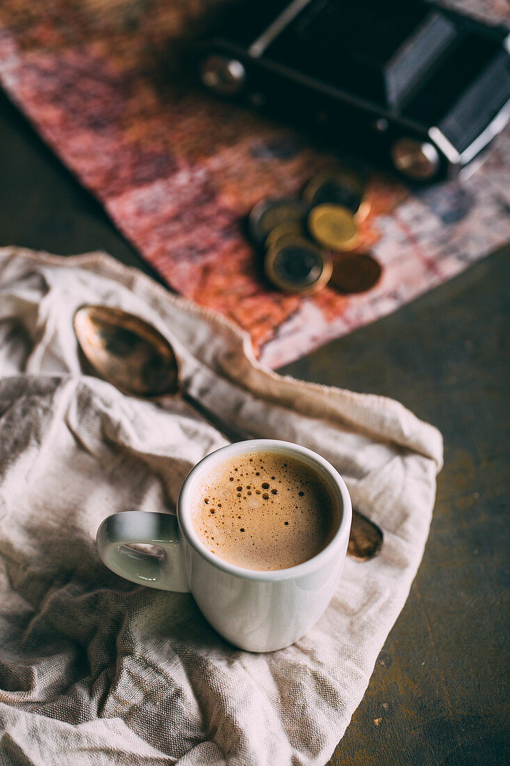 A cup of coffee on a cloth with a map, money and a model car in the background