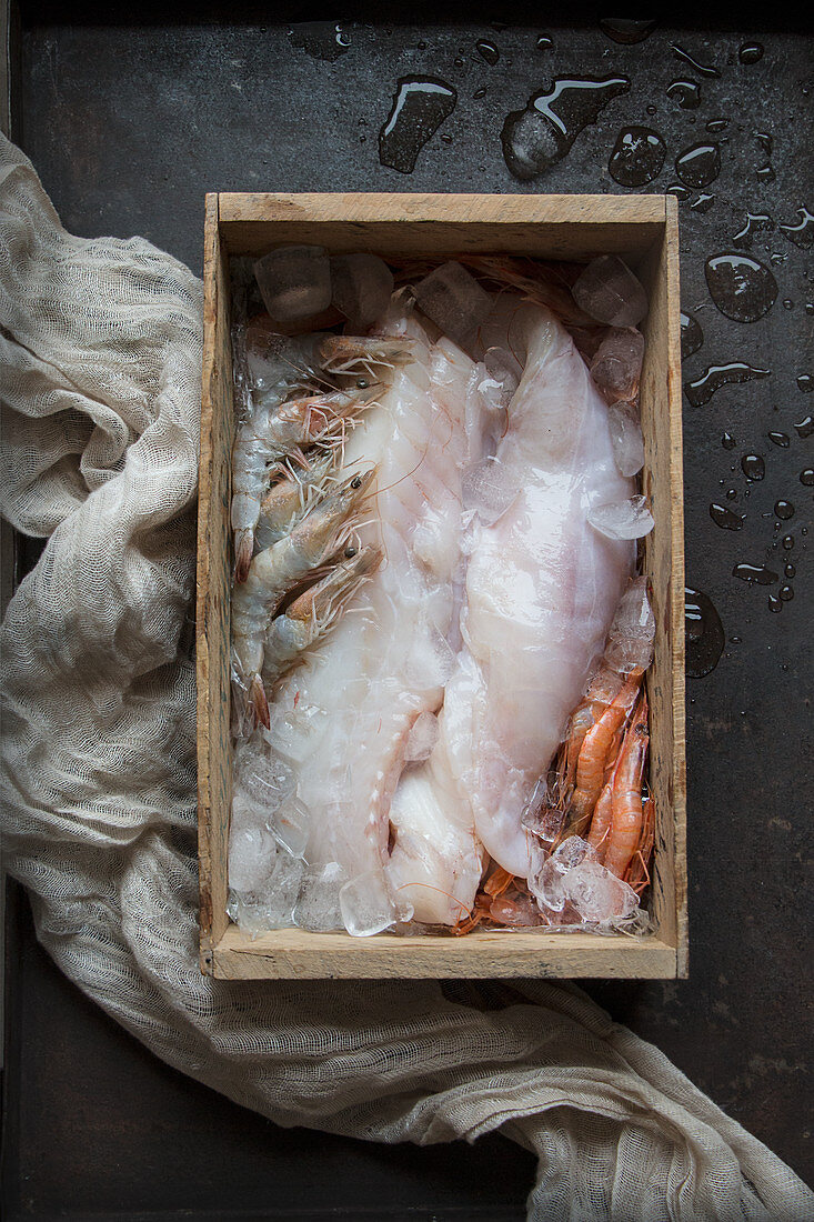 Rohe Fischfilets und Garnelen auf Eis in einer Holzkiste