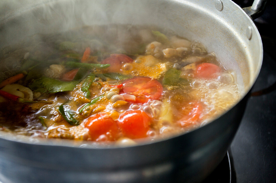 Preparing a Tom Yum Soup with mushrooms, chicken, lemongrass, chilis, kaffir lime leaves and tomatoes
