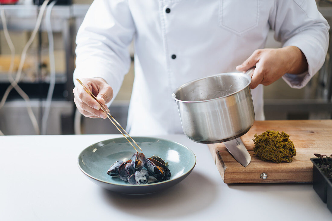 A chef serving cooked mussels on a plate