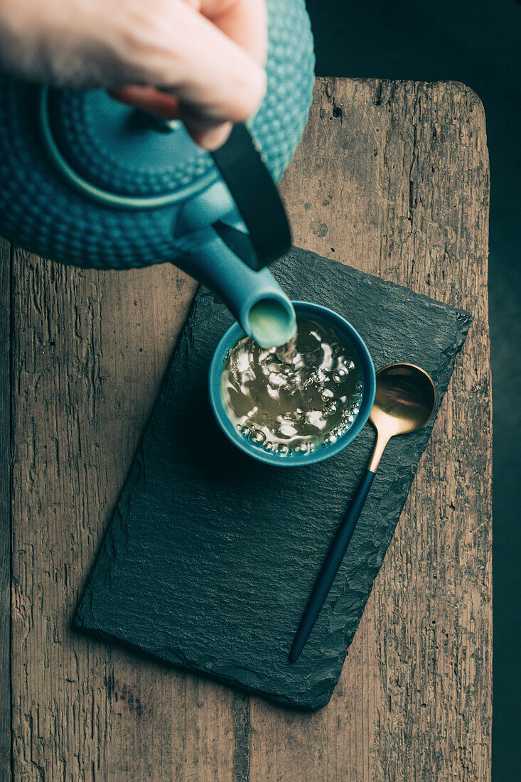 Tee aus asiatischer Teekanne in Teebecher einschenken