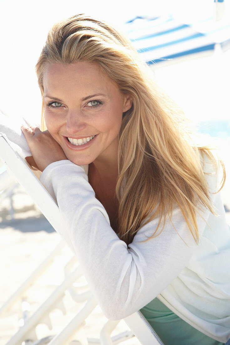 A blonde woman on a beach wearing a turquoise top and a white jacket