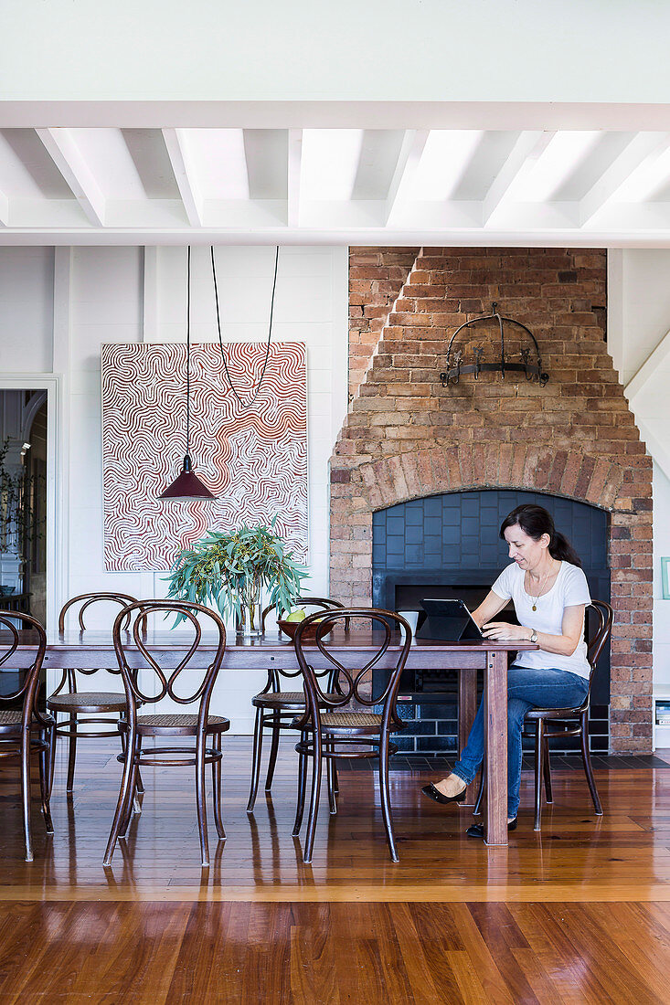 Dining area in front of rustic fireplace, woman with laptop at the table