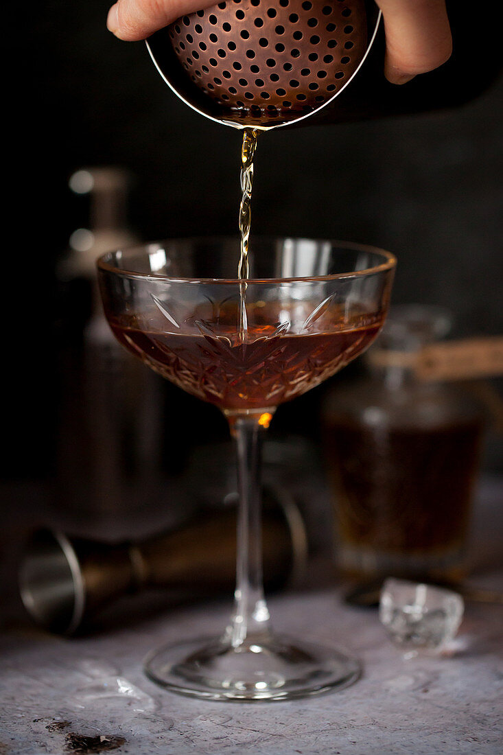 Ein Manhattan-Cocktail wird in ein Glas gegossen