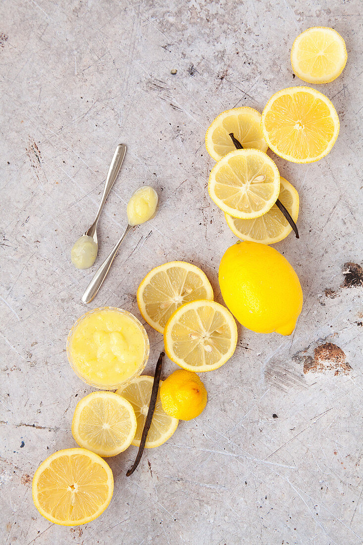 Lemon Curd mit Vanille in Gläschen und auf Löffeln umgeben von Zutaten
