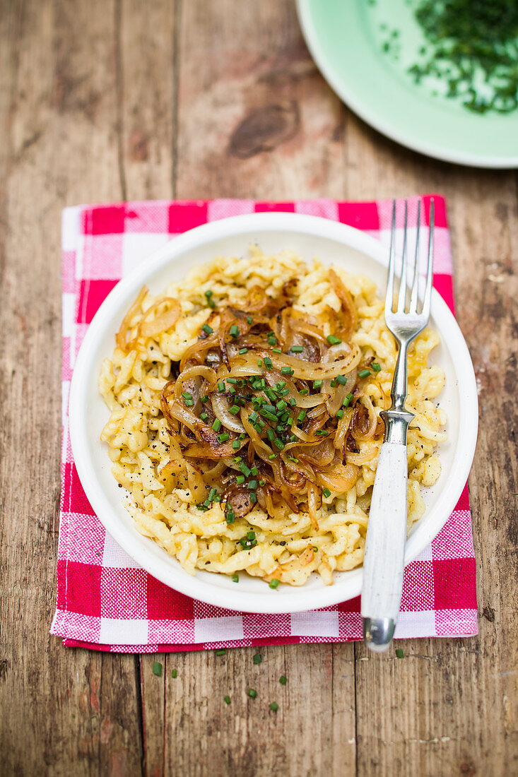 Cheese spaetzle with fried onions and chives on a wooden table