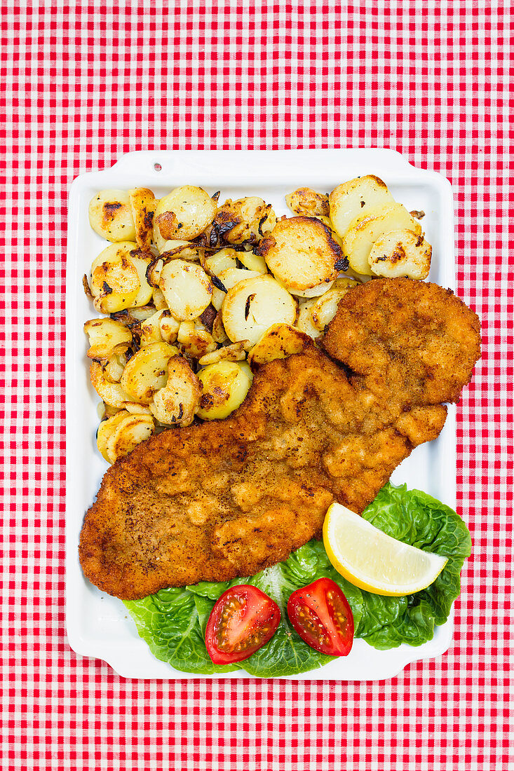 Breaded schnitzel with fried potatoes on a red and white checkered tablecloth