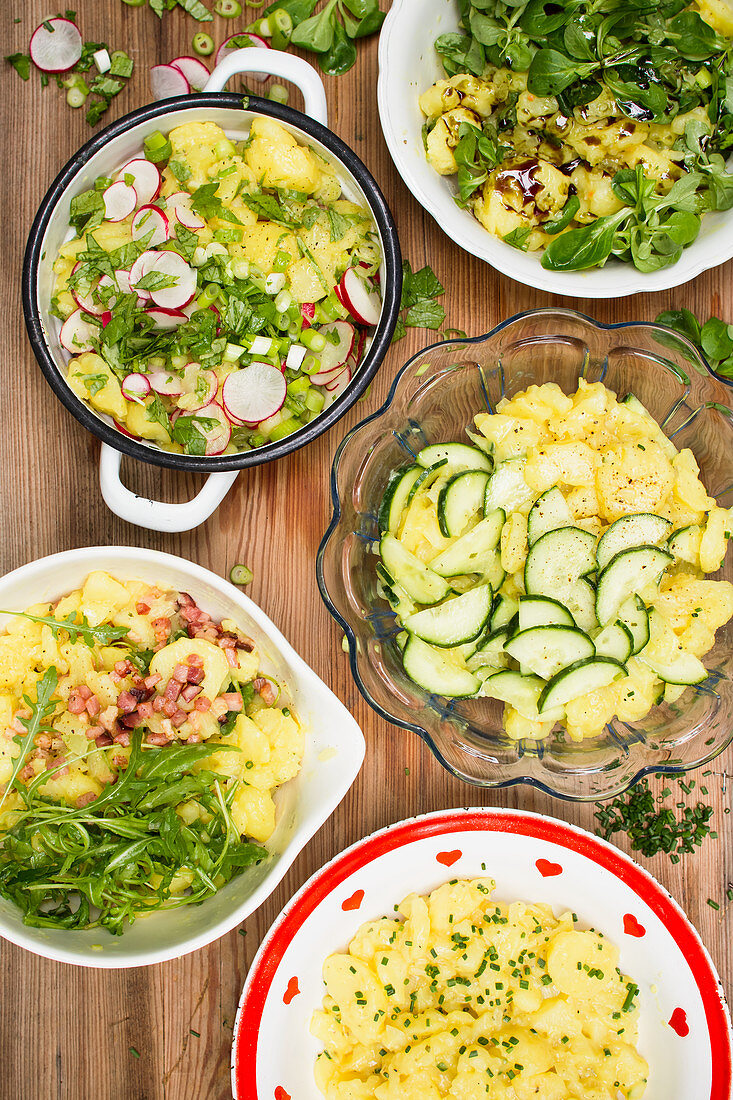 Various potato salads in bowls on a wooden background (top view)