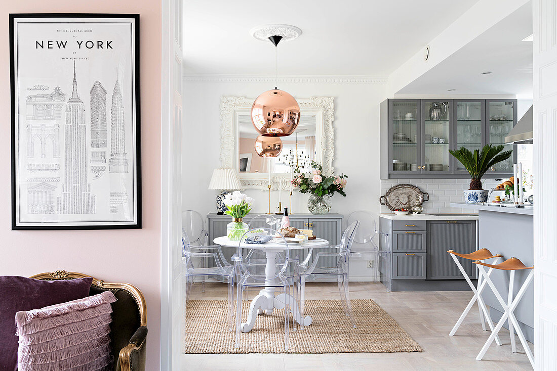 Open-plan kitchen with pale grey cupboards, round dining table and designer chairs with antique armchair and poster of New York in foreground