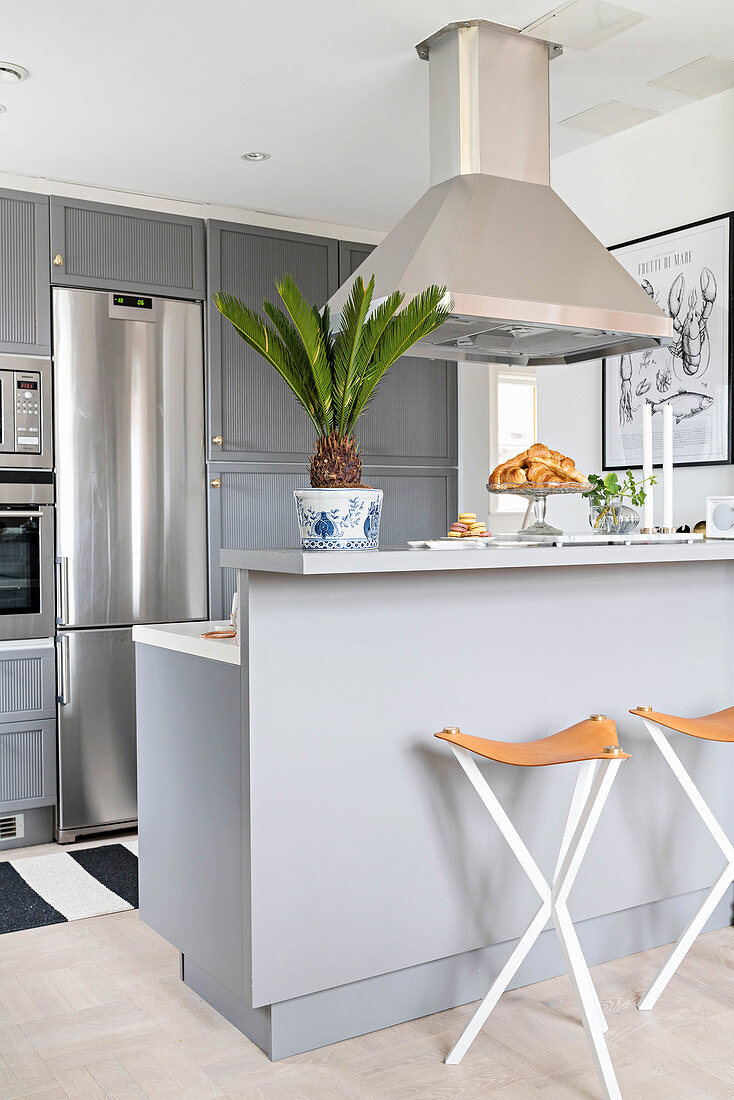 Pale grey counter and bar stools below extractor hood in open-plan kitchen