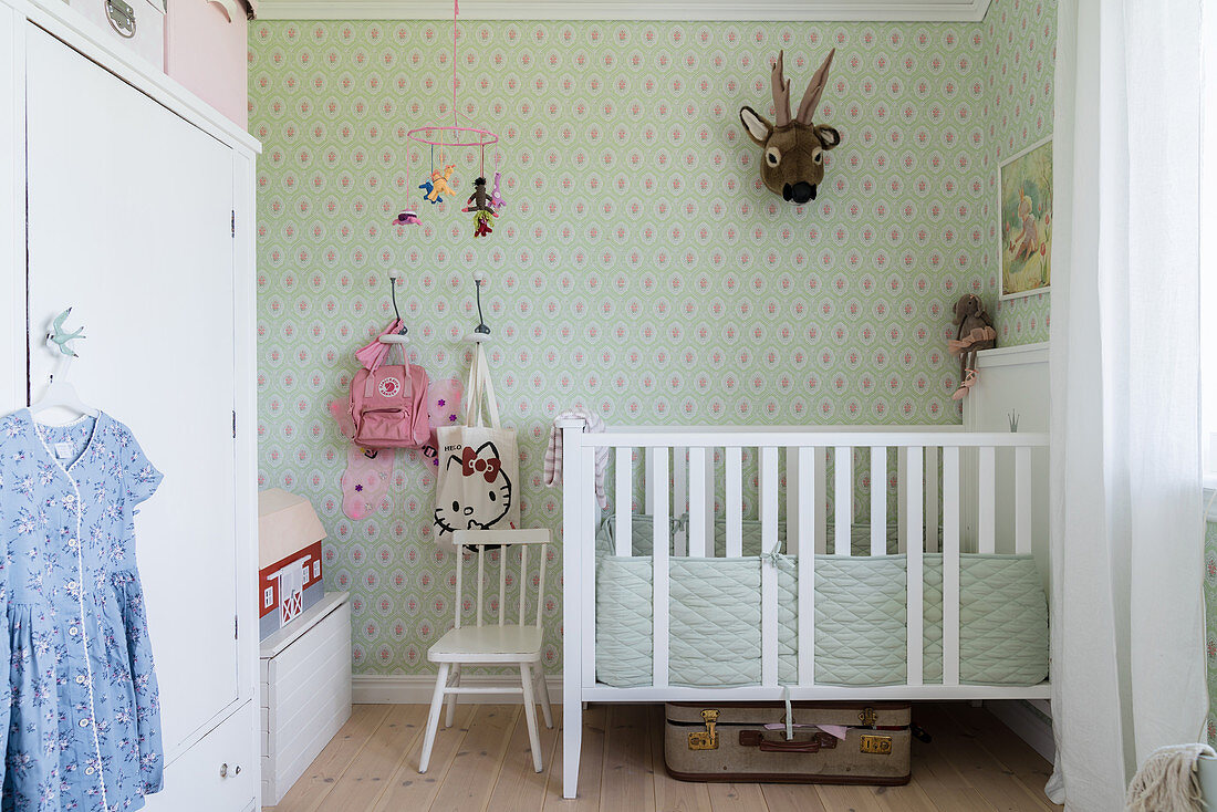 White cot, wardrobe and green wallpaper in nursery