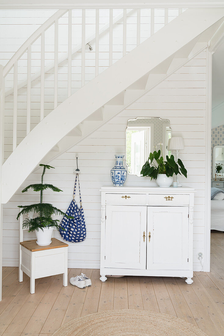 Cabinet against white wooden wall below staircase in foyer