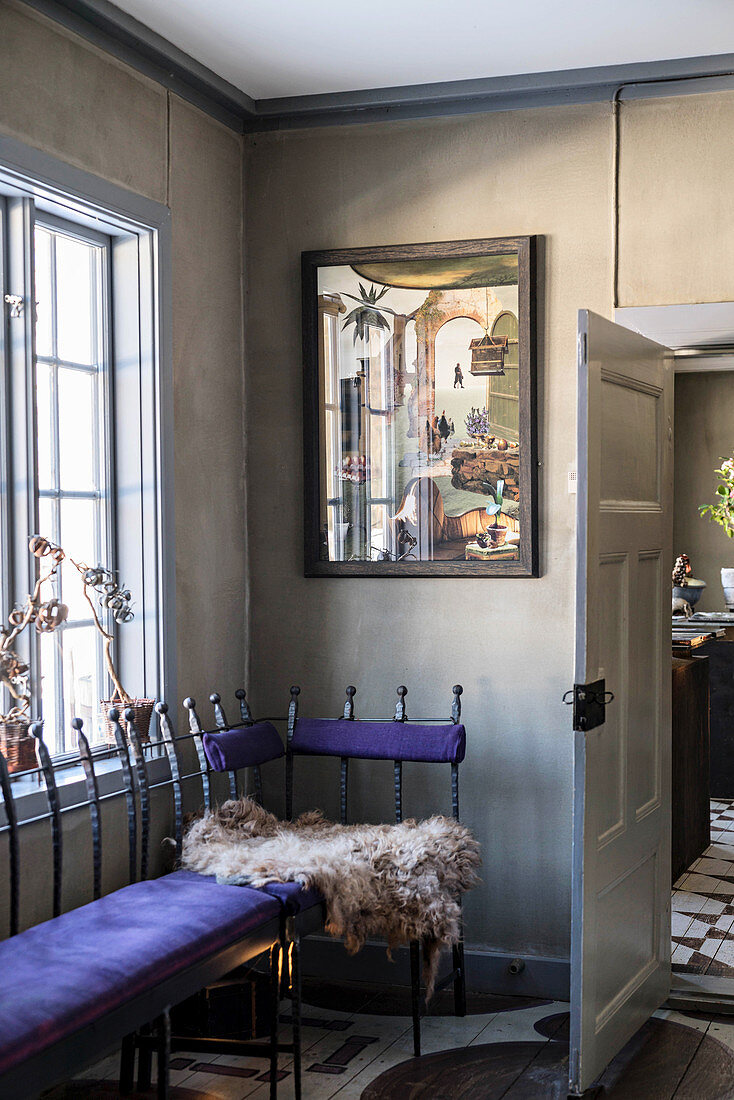 Metal bench with purple cushions in corner of room with artwork on grey-brown wall