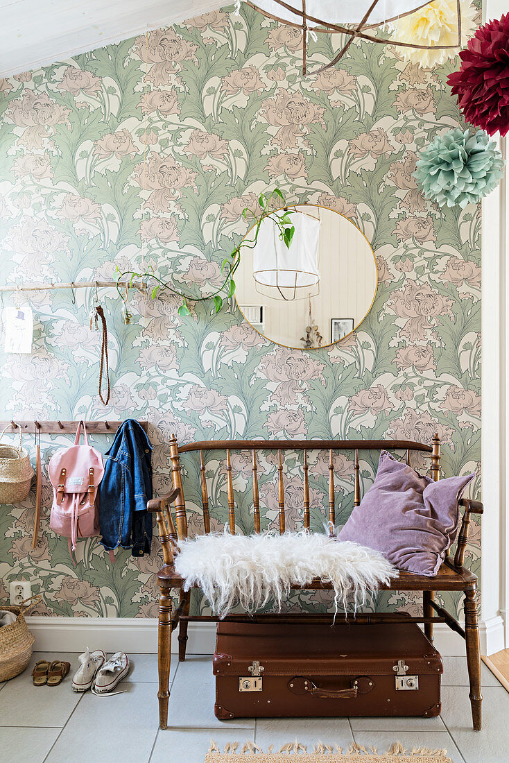 Old suitcase below spoke-back bench in front of floral wallpaper