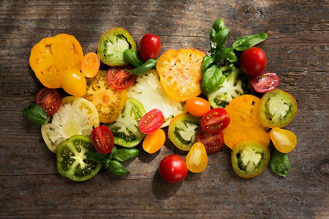 Various whole and sliced tomatoes with basil on a wooden board