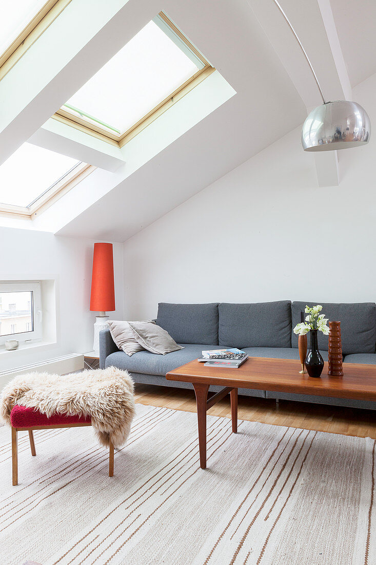 Grey sofa, coffee table and fur blanket on stool in attic living room