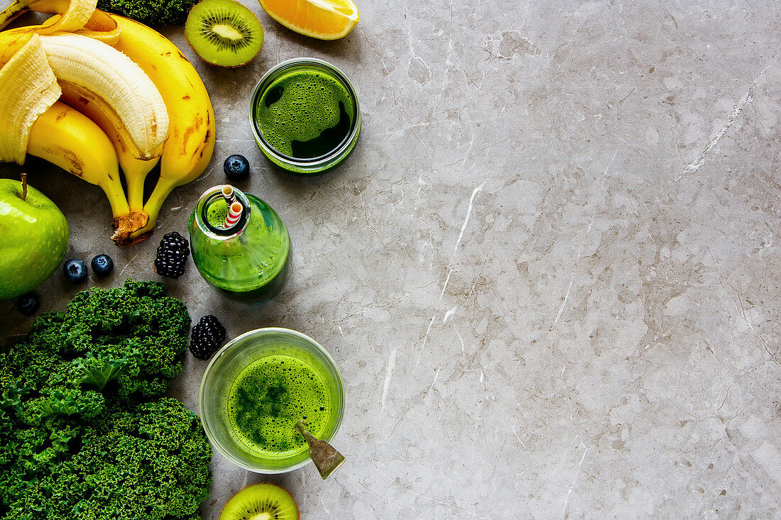 Grüner Detox-Smoothie in Flasche und Gläsern mit Zutaten auf grauem Untergrund