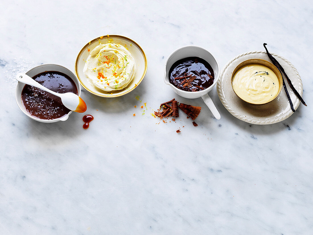 Verschiedene Pudding-Saucen: Salted-Caramel-Sauce, Hard Sauce mit Zitrusfrüchten, warme Fudge-Sauce, Creme Anglaise mit Bourbonvanille