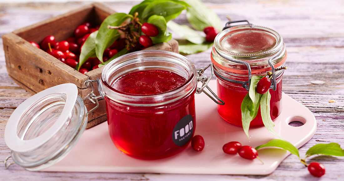 Homemade cornelian cherry jelly in glass jars on a wooden board