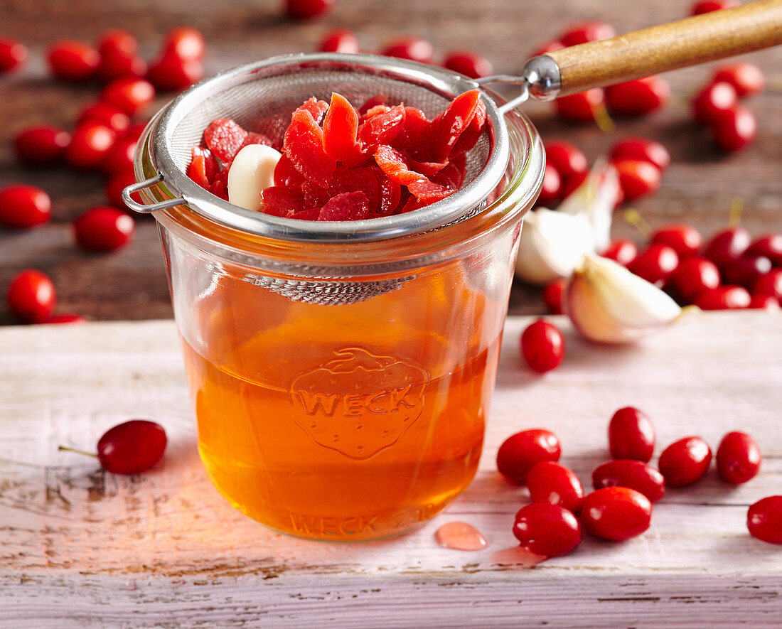 Homemade cornelian cherry vinegar with garlic and fruit vinegar in a mason jar with a strainer