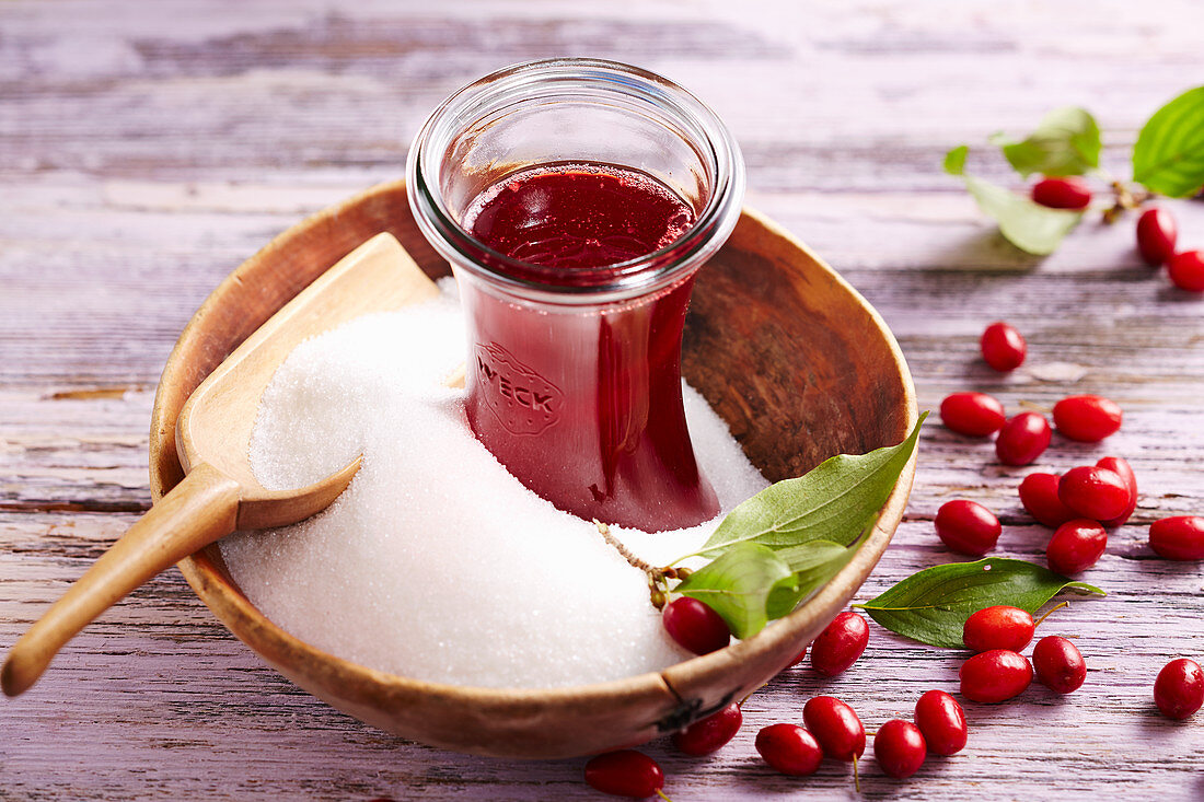 Flasche mit selbstgemachtem Kornelkirschen-Sirup in Holzschale mit Zucker