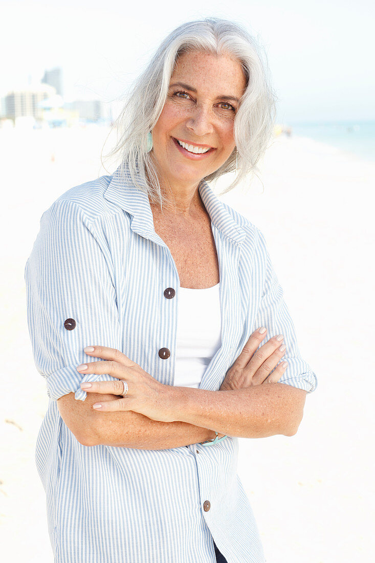 A mature woman with white hair on a beach wearing a striped blouse and a top