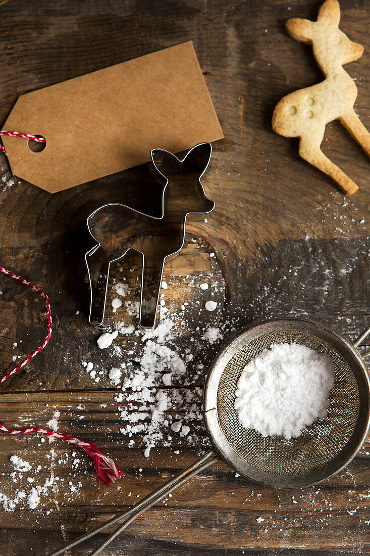 Festive Christmas baby deer biscuit with cookie cutter and icing sugar in sifter and gift tag