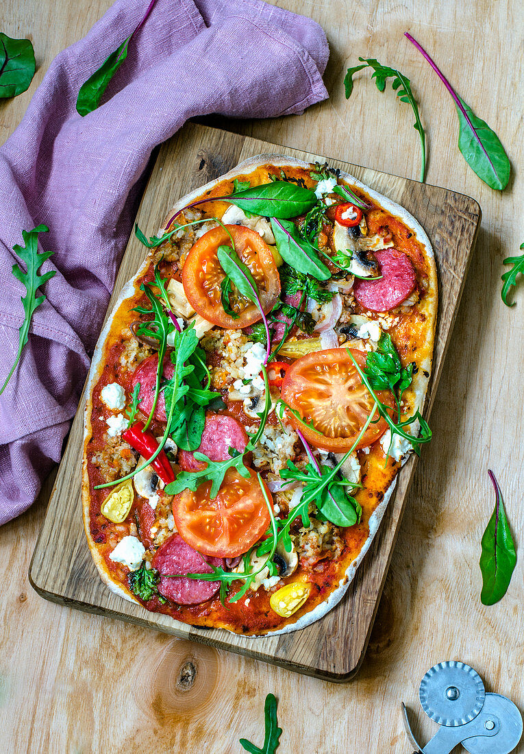 Pizza with salami, mushrooms, feta, tomatoes and greens