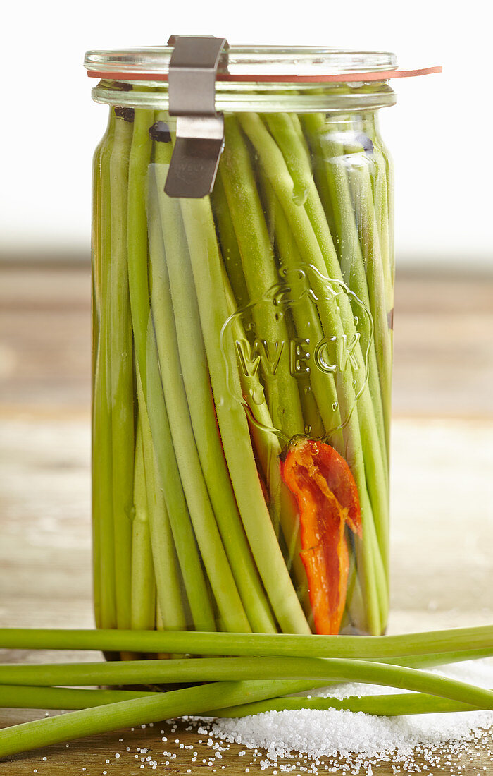 Pickled long green garlic shoots in a jar of salted water with chilli and pepper