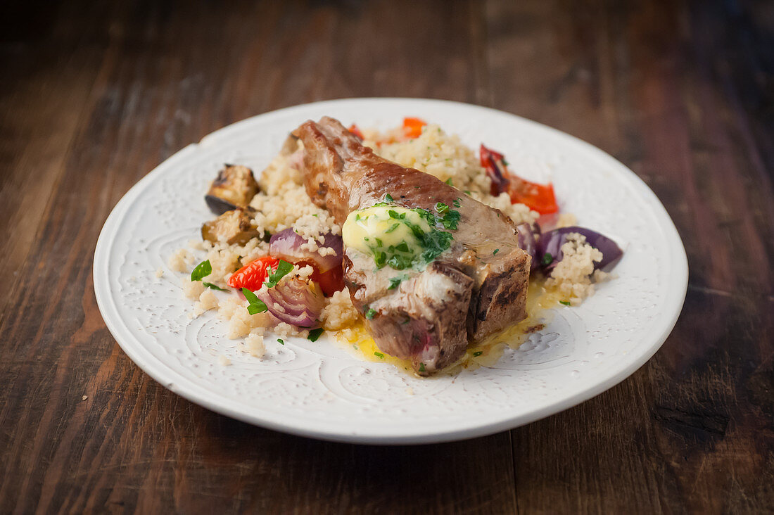A pork chop with herb butter, couscous and vegetables