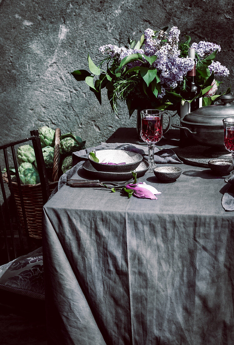Gedeckter Tisch mit Rotwein, Flieder und Artischocken