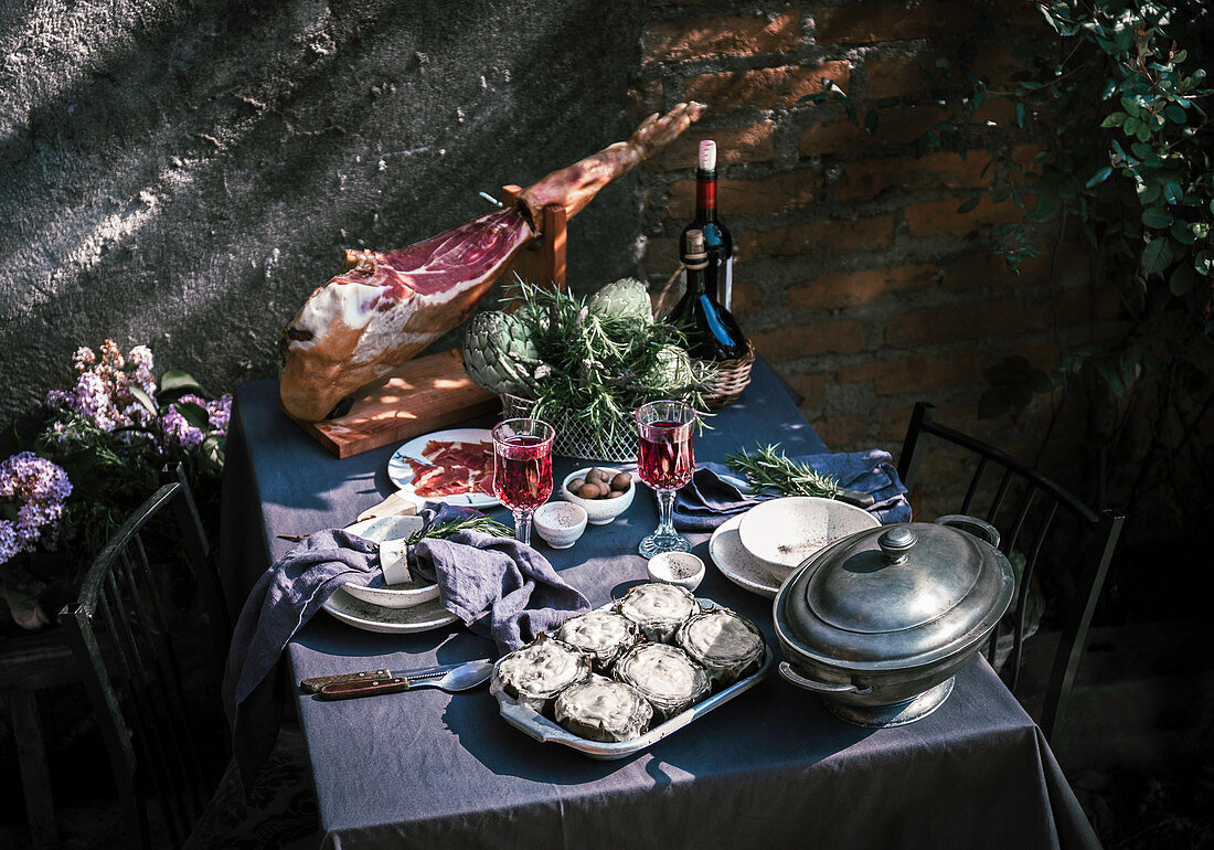 Gedeckter Tisch mit Rotwein, Artischocken und Serranoschinken