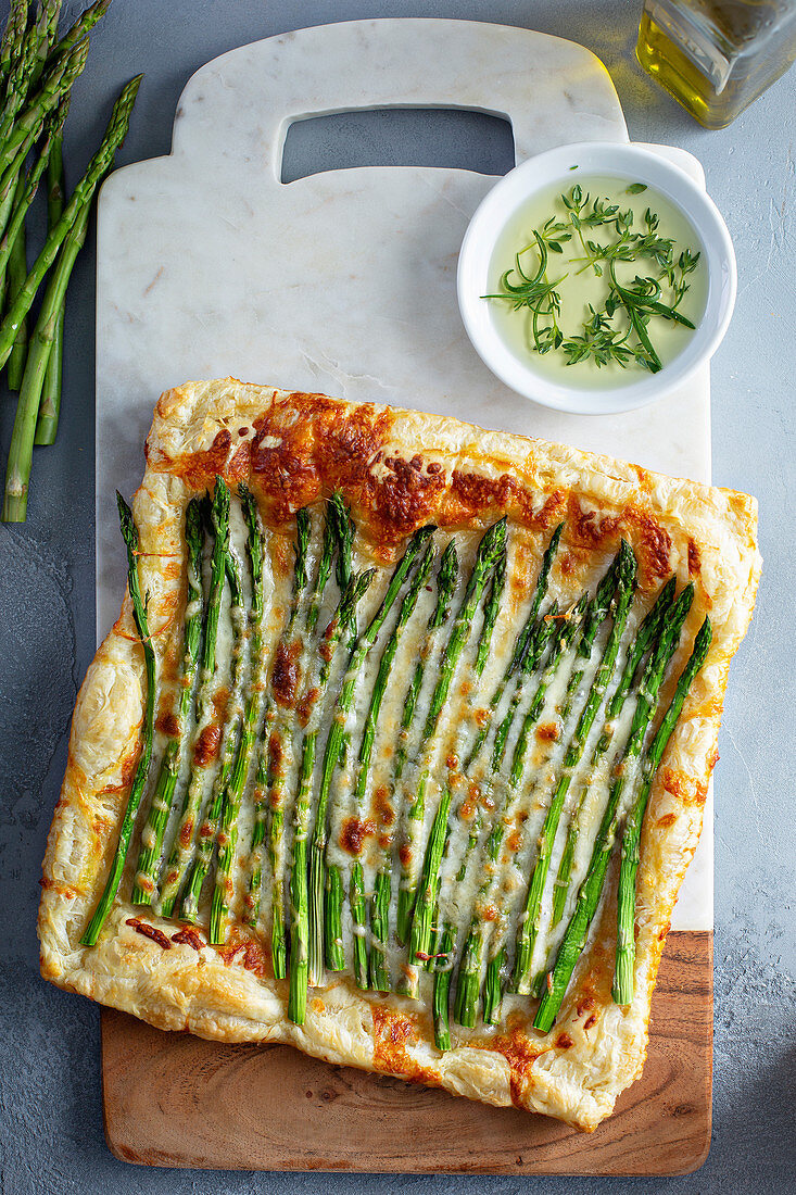 Blätterteigtarte mit grünem Spargel und Käse serviert mit Kräutern und Olivenöl