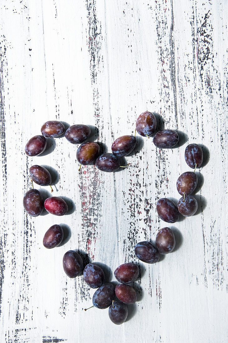 Damsons arranged in a heart-shape on a rustic wooden surface