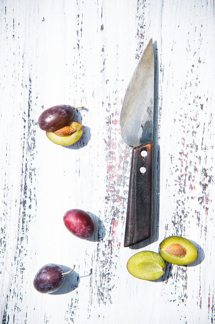 Damsons sliced and whole with a knife on a rustic wooden surface