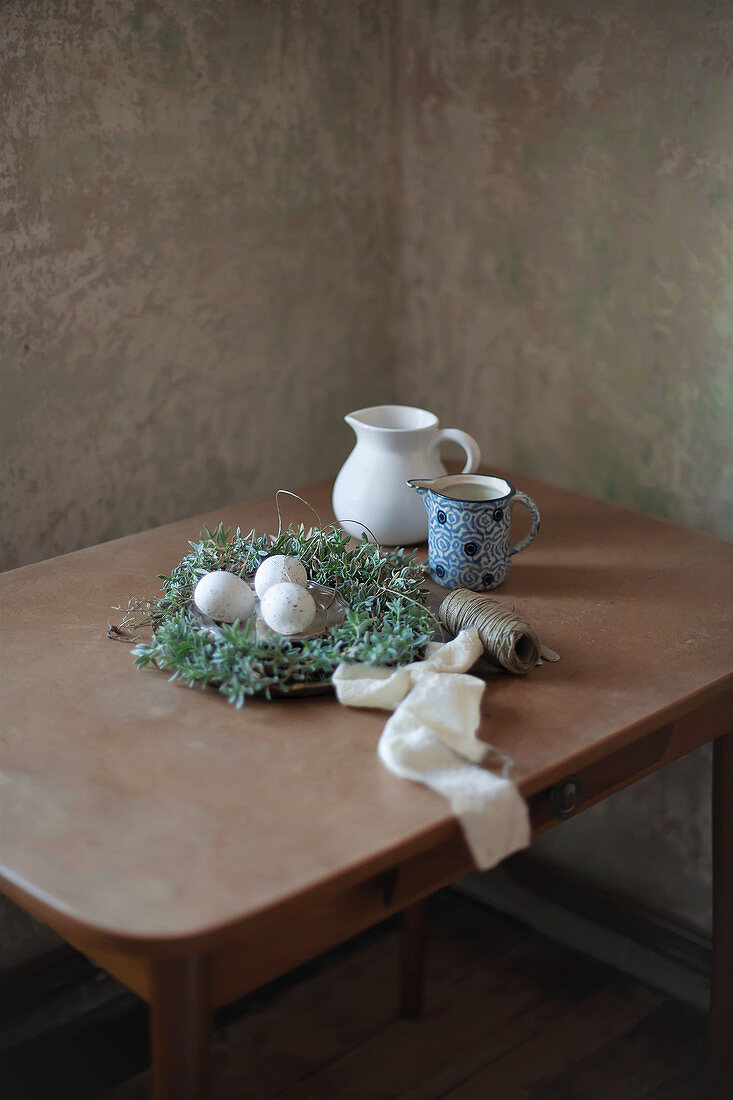 Speckled eggs in Easter nest and jugs on table