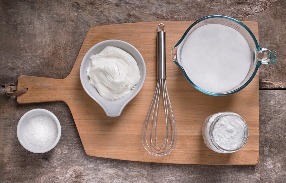 White frosting and ingredients on light cutting board and light rustic wood surface