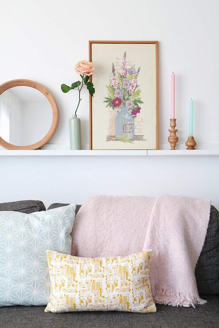 Ornaments on narrow shelf above pastel cushions on sofa