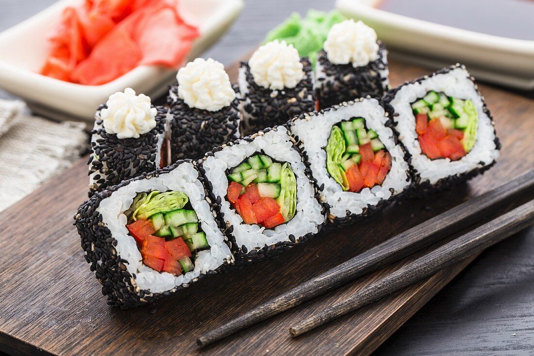 Sushi-Rollen mit schwarzen Sesamsamen, Lachs, Garnelen und Tomaten