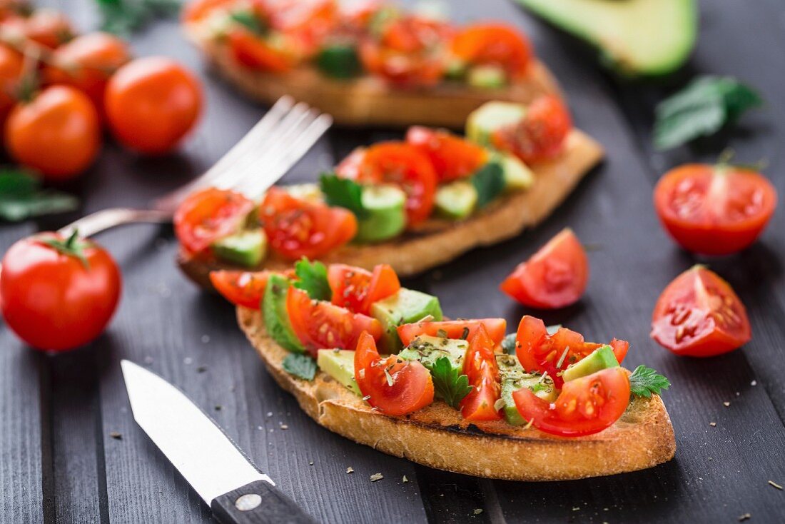 Bruschetta with tomato, avocado and herbs on a black wooden table