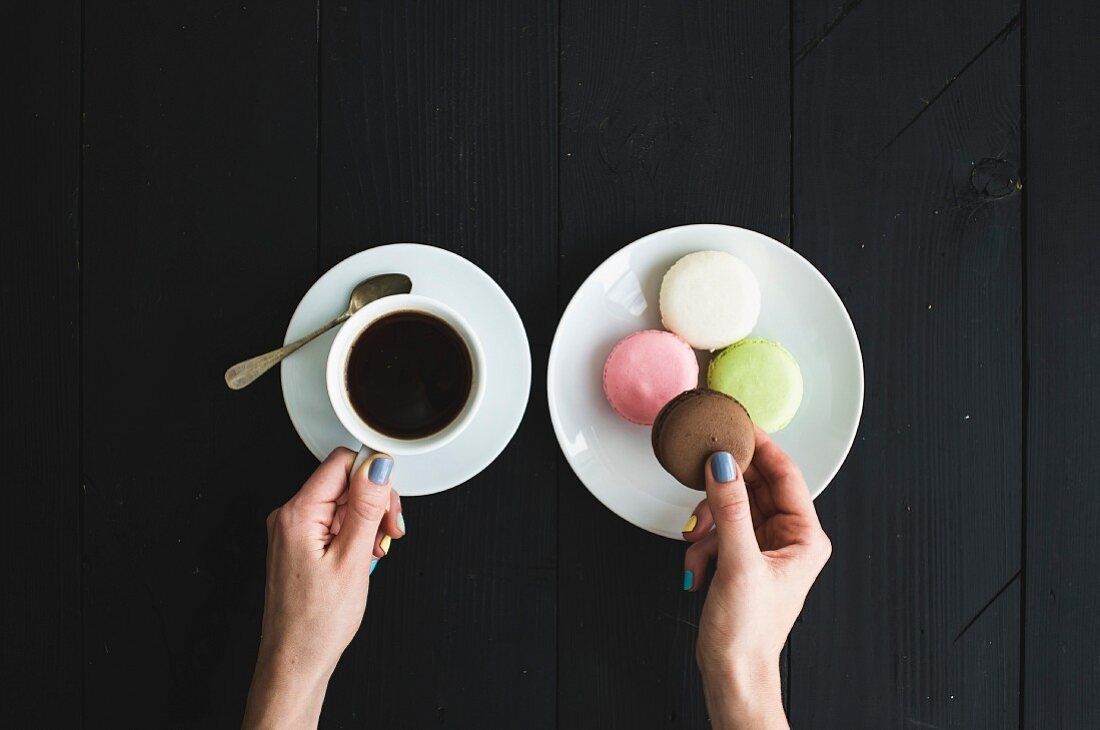 Frauenhände halten eine Tasse Espresso und Macaron