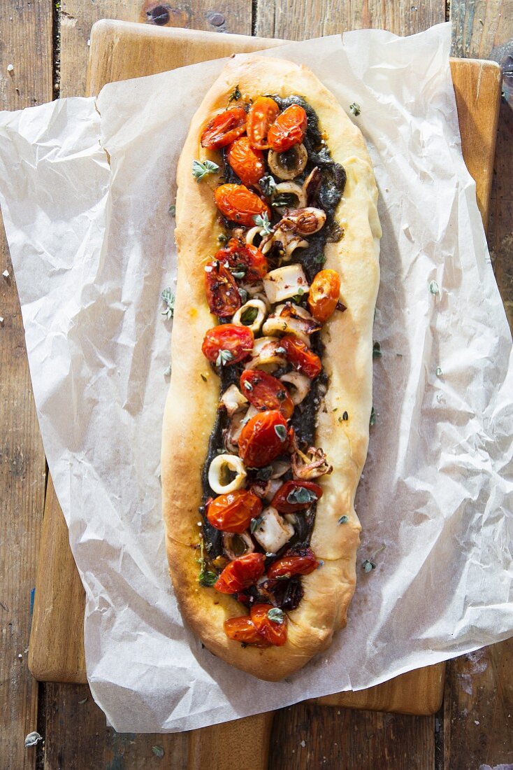 An oval-shaped flatbread pizza with squid and cherry tomatoes