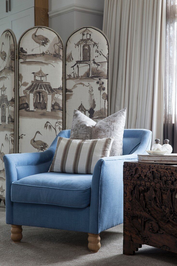 Blue armchair with beige scatter cushions in front of upholstered screen