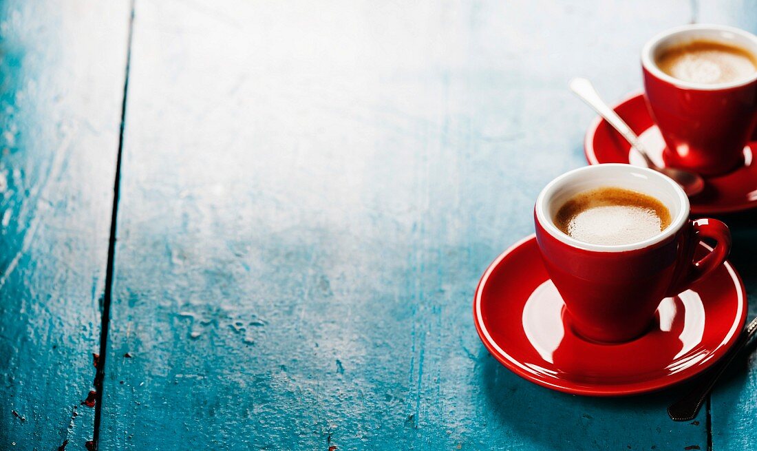 Zwei rote Espressotassehn auf blauem Holzuntergrund