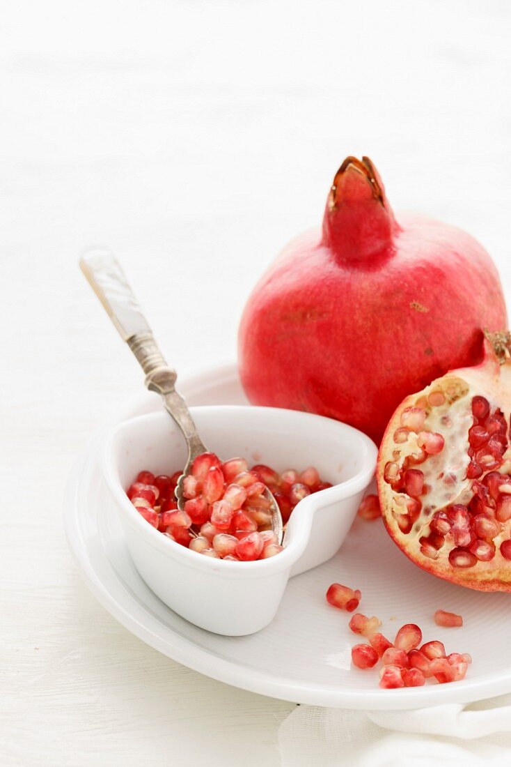 Pomegranate Seeds, some peeled and whole on a white background