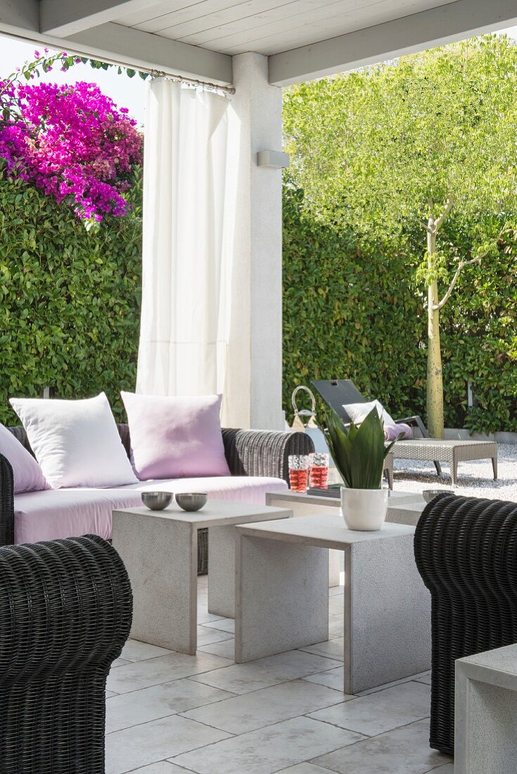 Überdachte elegante Terrasse vor Hecke mit blühender Bougainvillea