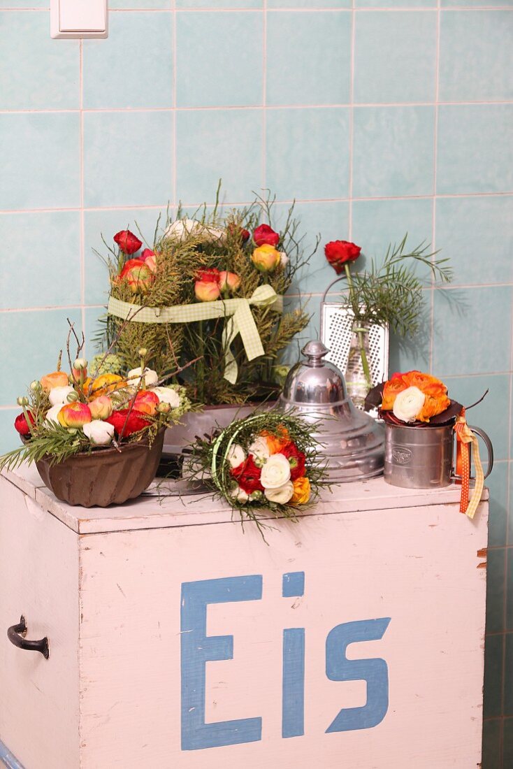 Blumengestecke in Küchenutensilien auf einem alten Eiswagen