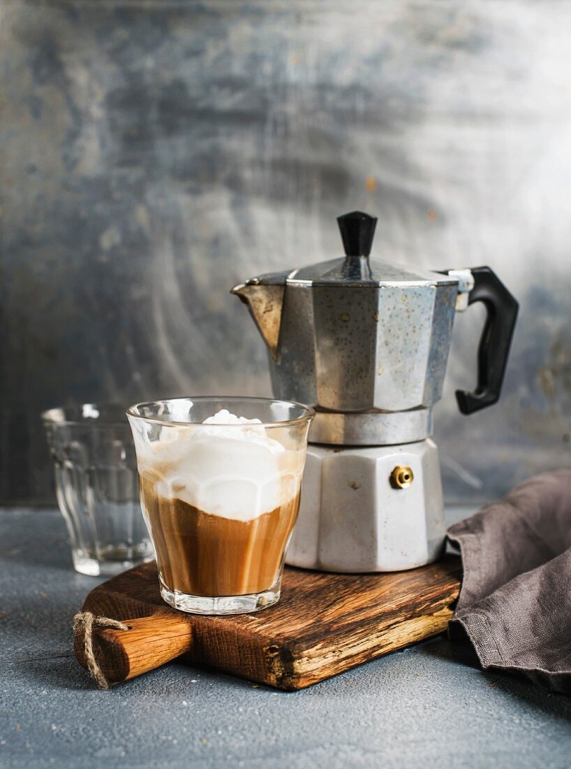 Kaffee mit Eis in einem Glas und Espressokanne auf rustikalem Holzbrett