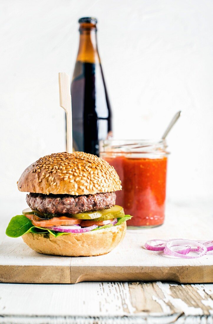 Fresh homemade burger on wooden serving board with spicy tomato sauce and bottle of dark beer
