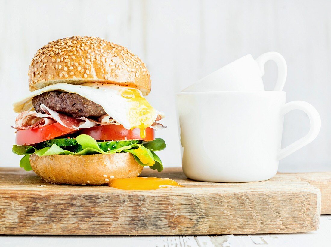 Breakfast set: Homemade beef burger with fried egg and vegetables and coffee cups on wooden board